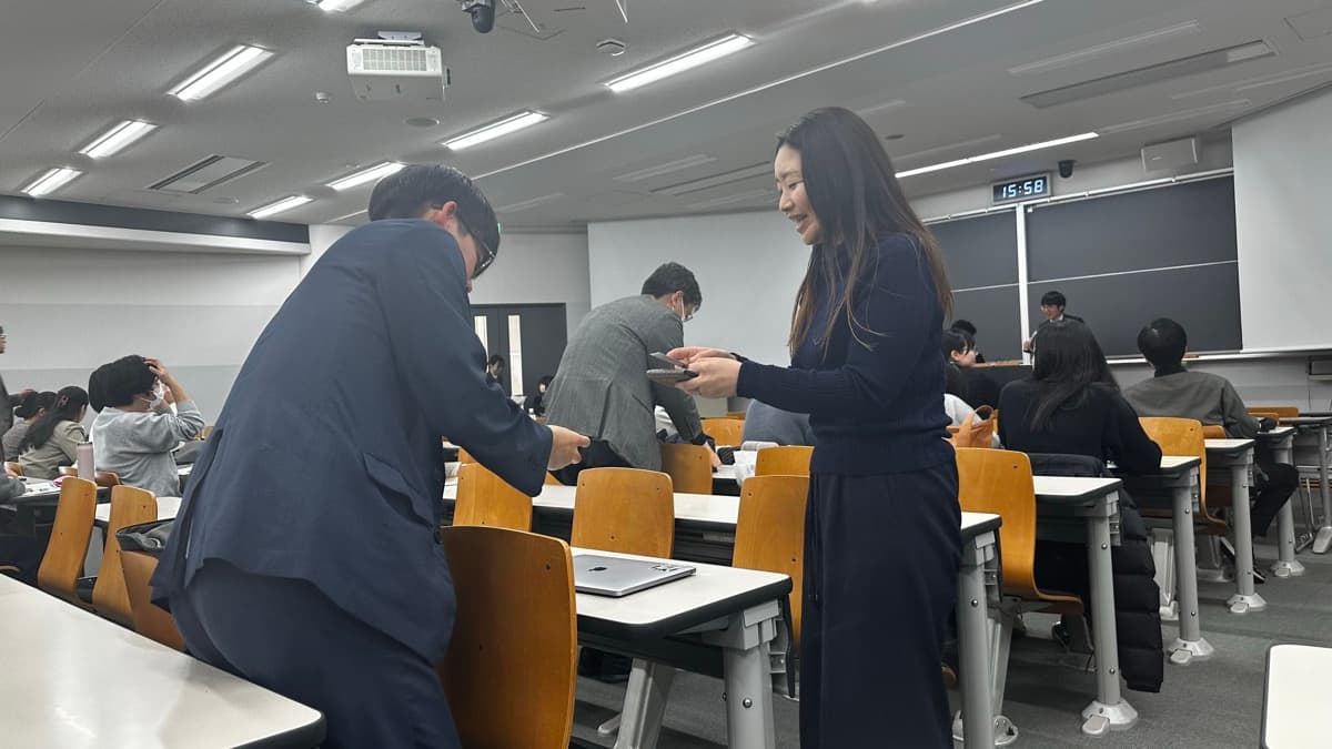 Two people exchanging business cards at the venue of the Student Community Activity Report in Bunkyo-ku