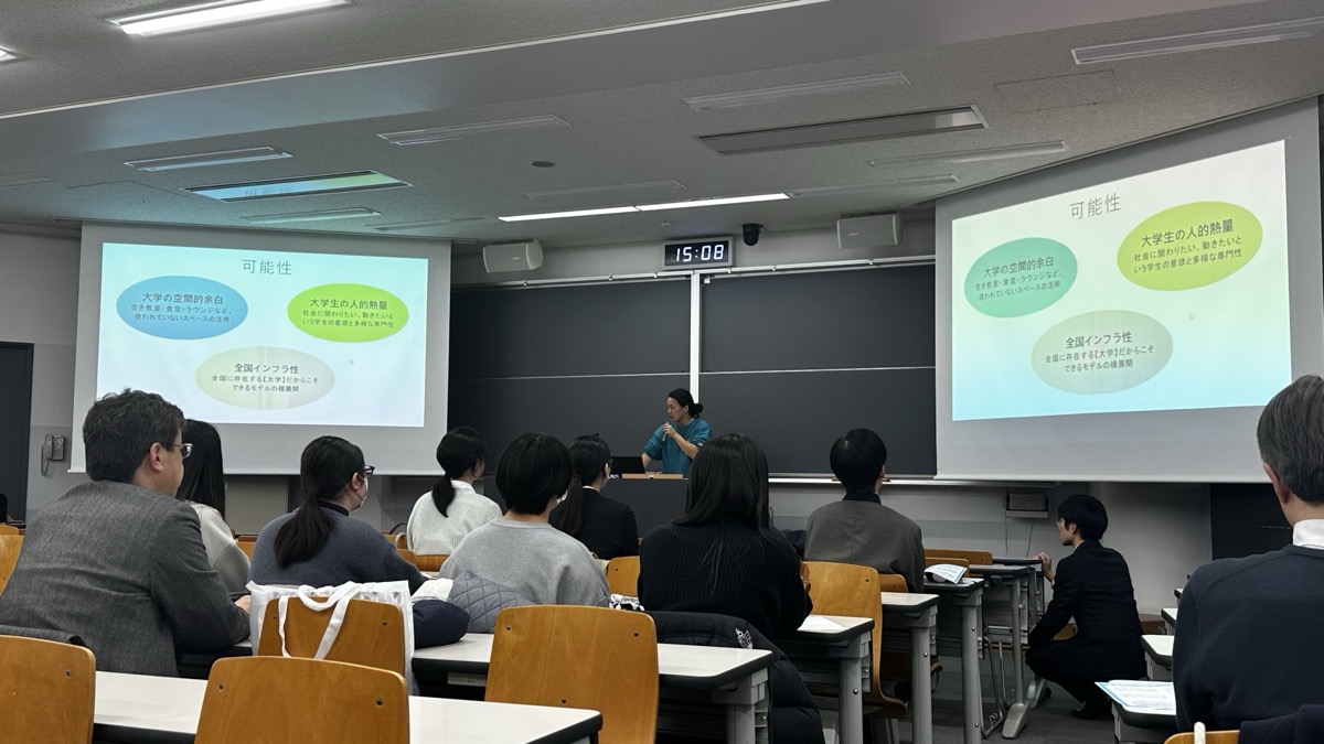 「学生による地域活動報告会 in 文京区」で、講義室の画面に発表の資料が映り、参加者が聞いている